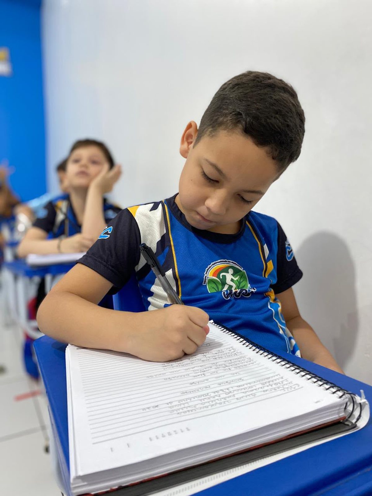 Aluno do Colégio CIEC escrevendo no caderno em sala de aula